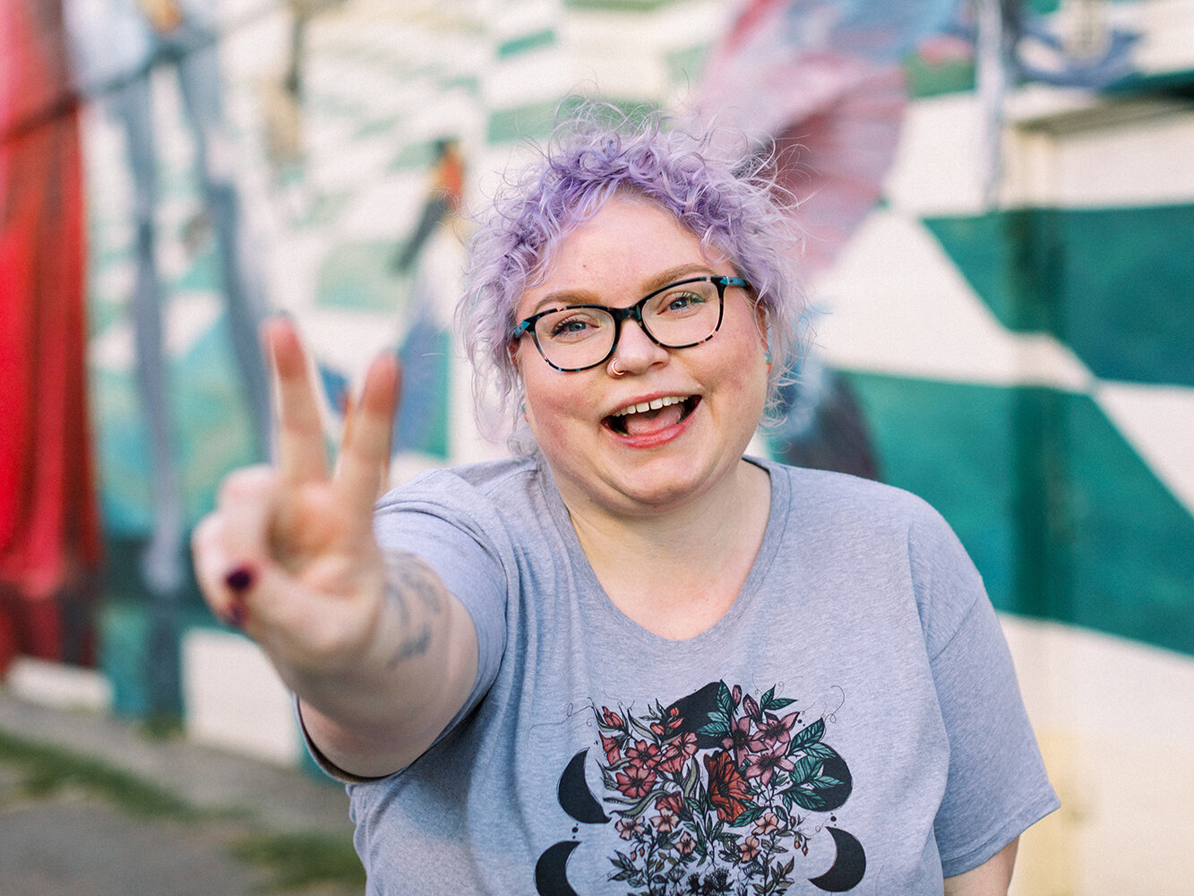 a woman with short curly purple hair is giving a peace sign with her hand and smiling