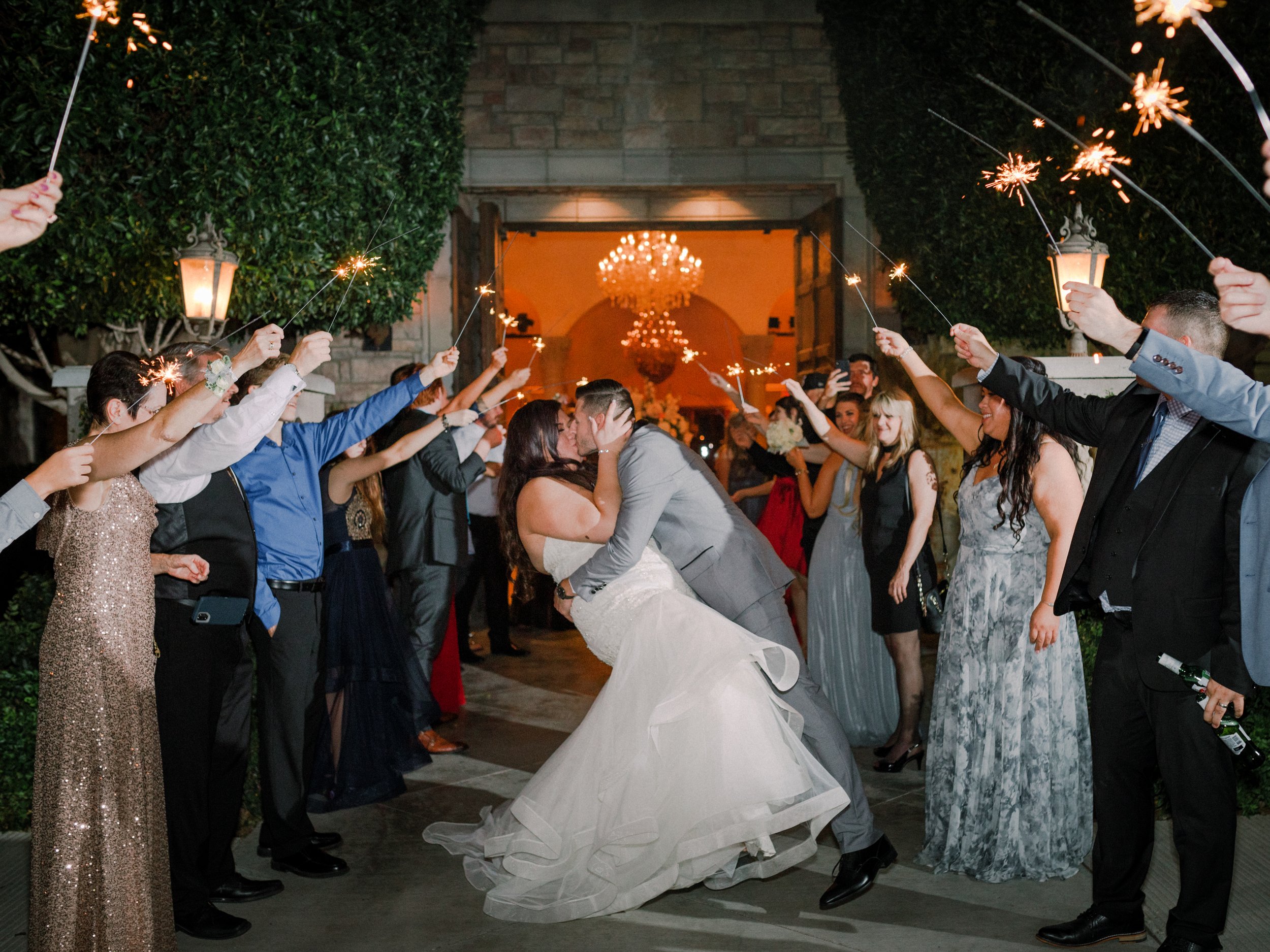 the groom dips the bride and kisses her under sparklers their wedding guests are holding up