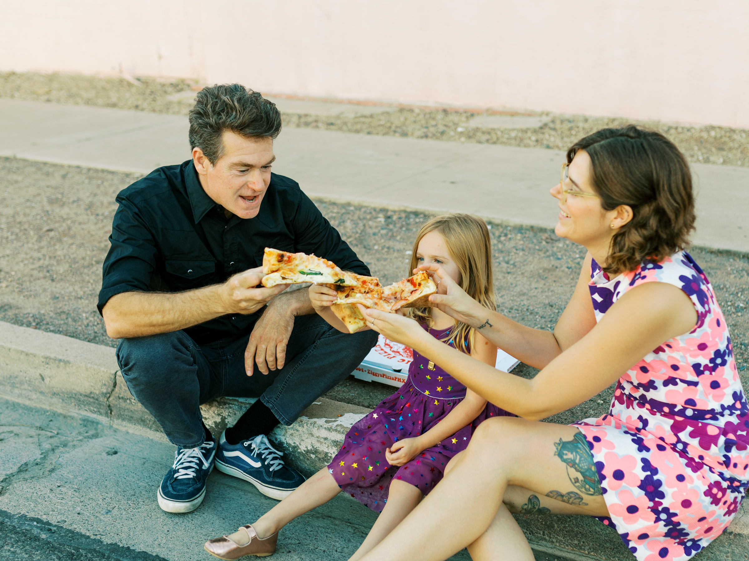 family sits on curb eating ziggy's pizza