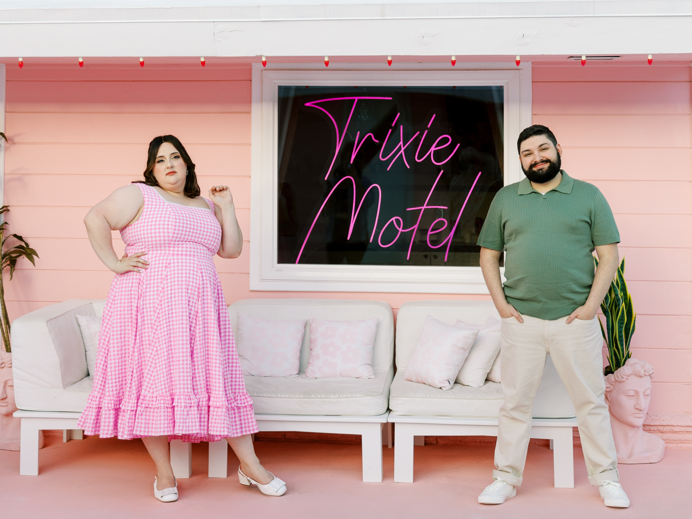A couple stands on either side of the window with the neon Trixie Motel sign