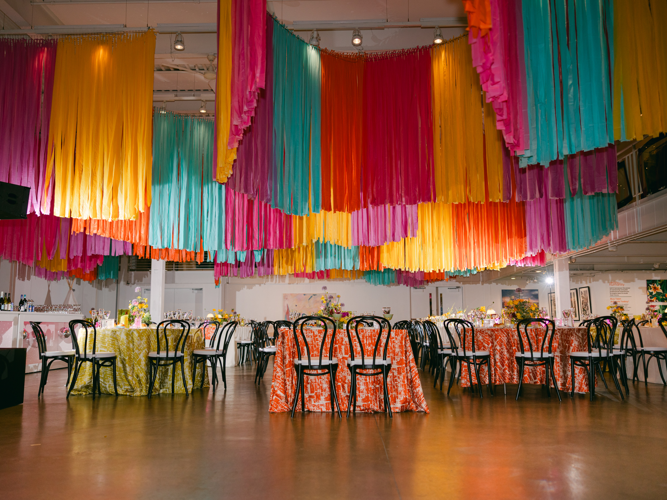 colorful streamers hang from ceiling installation over mismatched reception tables in bright orange and lime green